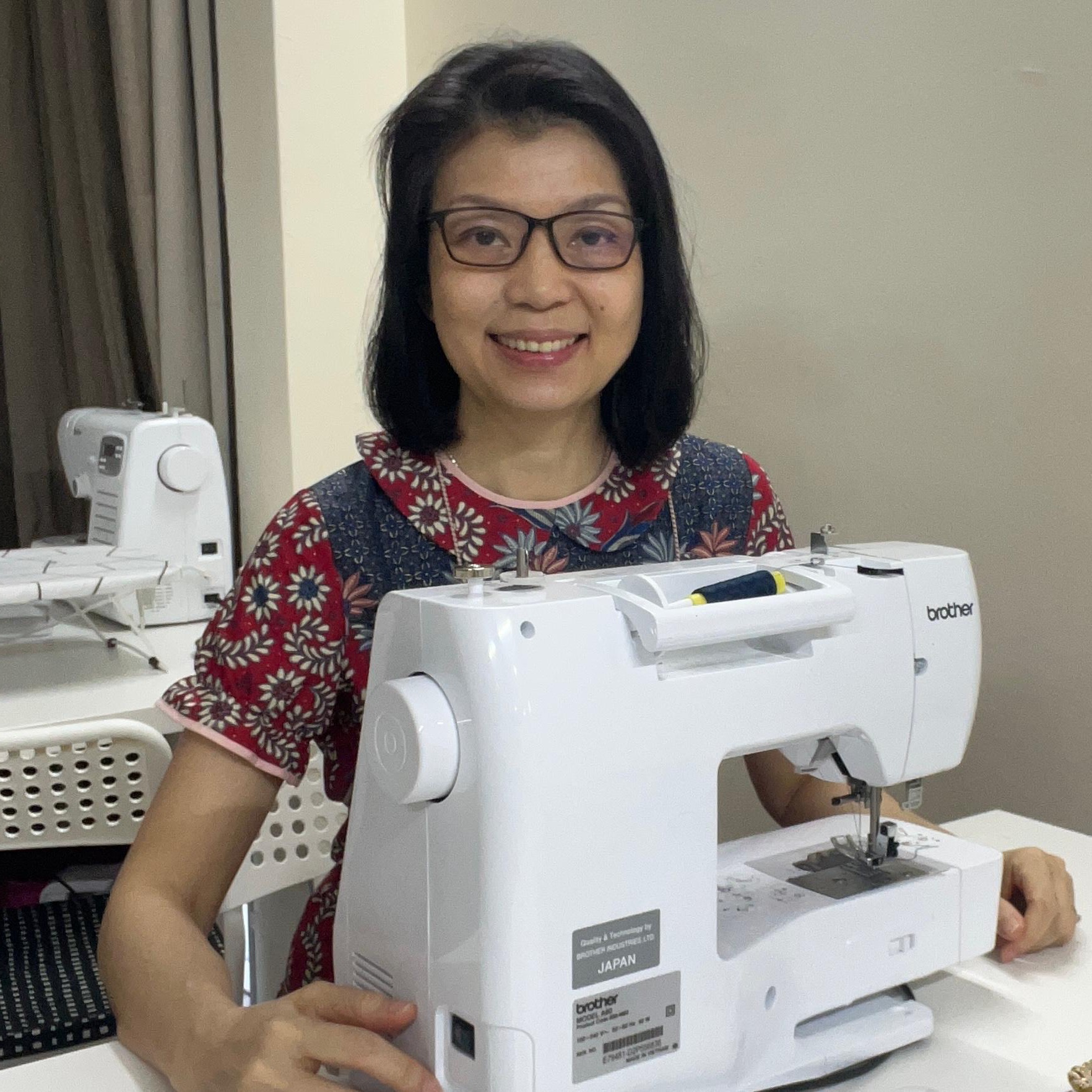Angela Pok, founder of Two Moles, smiling behind a sewing machine in the studio